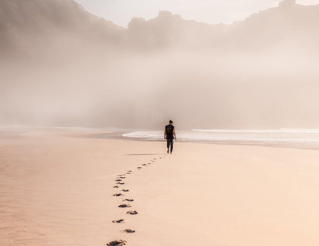 anonymous man walking on sandy seashore in misty weather