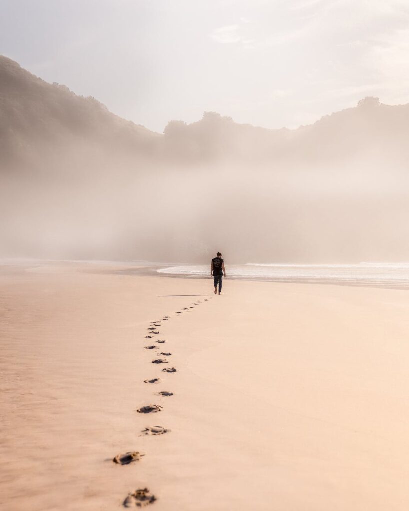 anonymous man walking on sandy seashore in misty weather